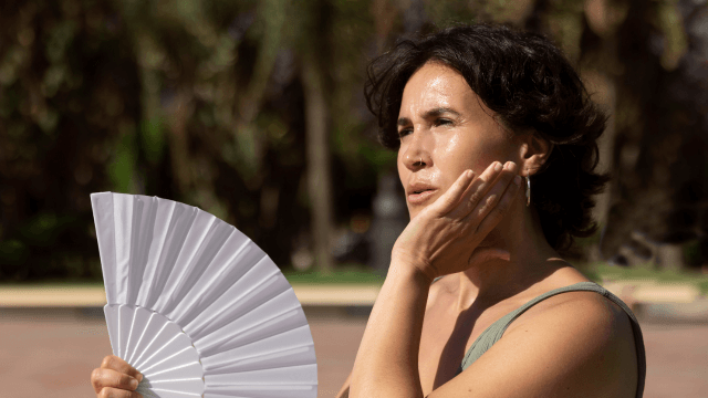 Une personne au soleil tenant un ventilateur pour éviter la surchauffe