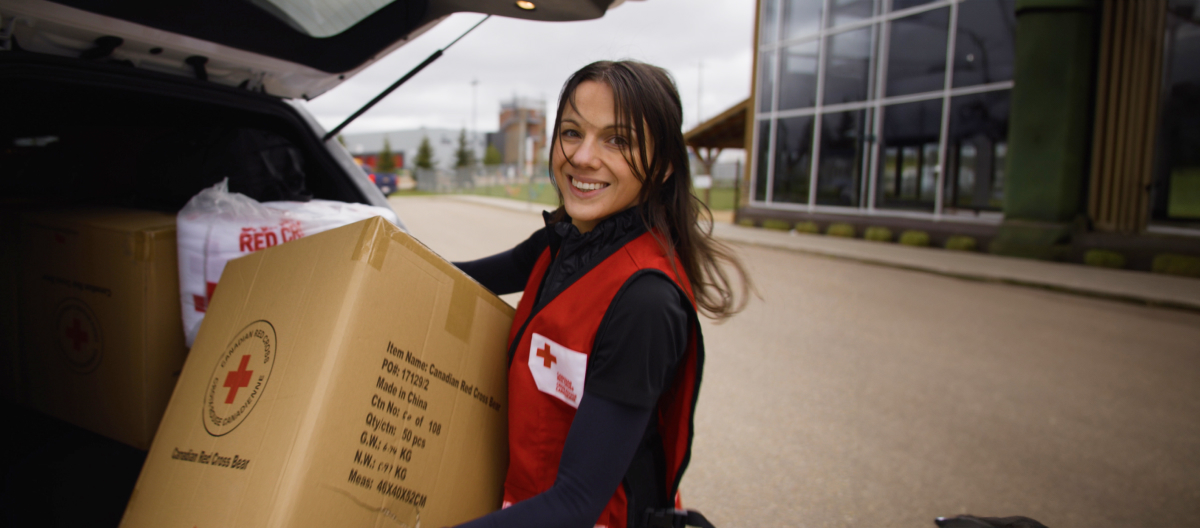 Une employée de la Croix-Rouge transporte une boîte de fournitures en souriant.