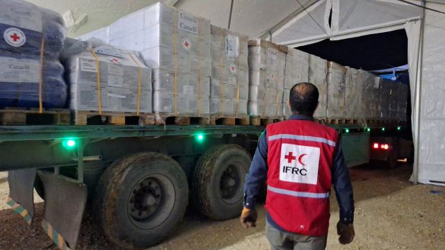 Un membre du personnel de la FICR se tient devant un camion contenant des aides humanitaires.