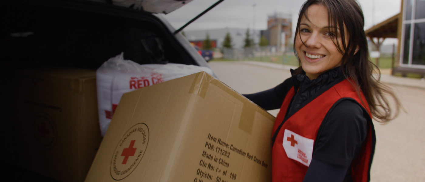 Une employée de la Croix-Rouge transporte une boîte de fournitures en souriant.