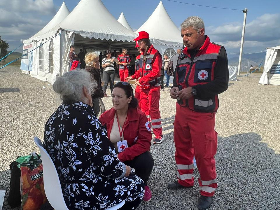 Un groupe de personnes portant des vêtements de la Croix-Rouge s’occupe d’une femme aînée assise