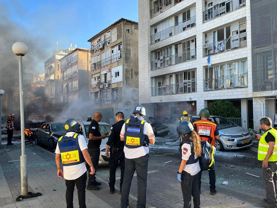 Un groupe de personnes est debout devant des immeubles avec de la fumée en arrière-plan.